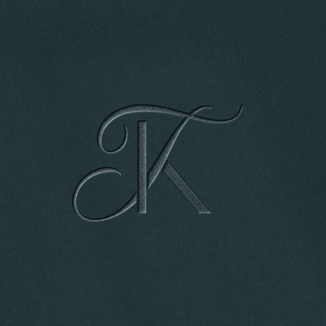 Embossed KT and TK letter logo as premium initials design on blue background for luxury wedding stationery and quality print